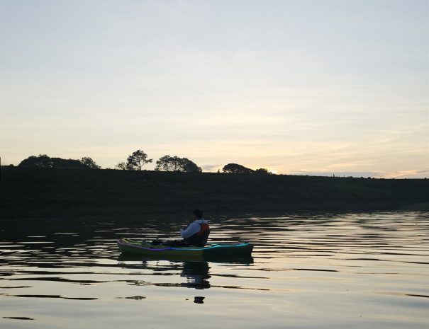 Una persona en kayak sobre la presa durante el amanecer, con reflejos de luz en el agua