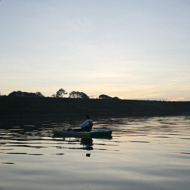 Una persona en kayak sobre la presa durante el amanecer, con reflejos de luz en el agua