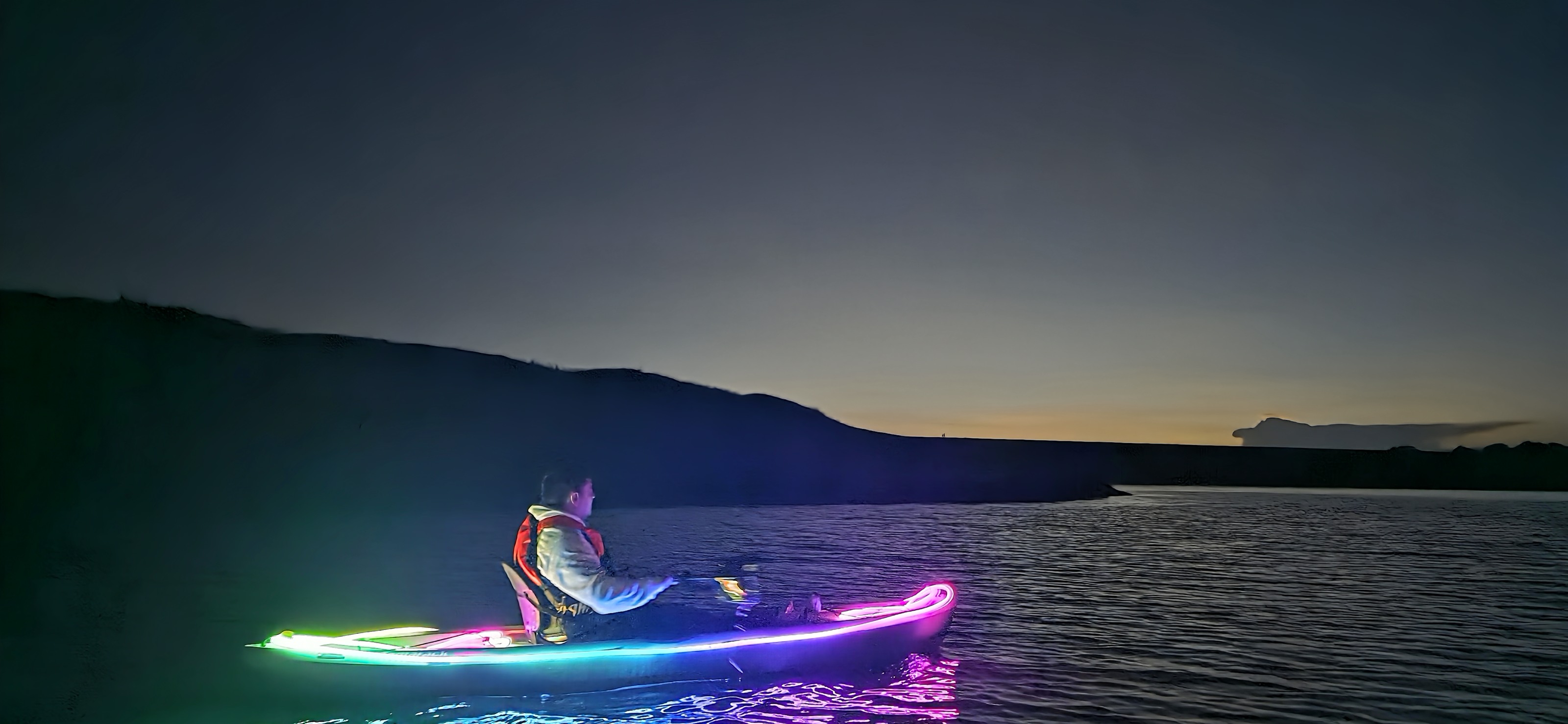 Persona en kayak iluminado con luces de colores durante la hora azul